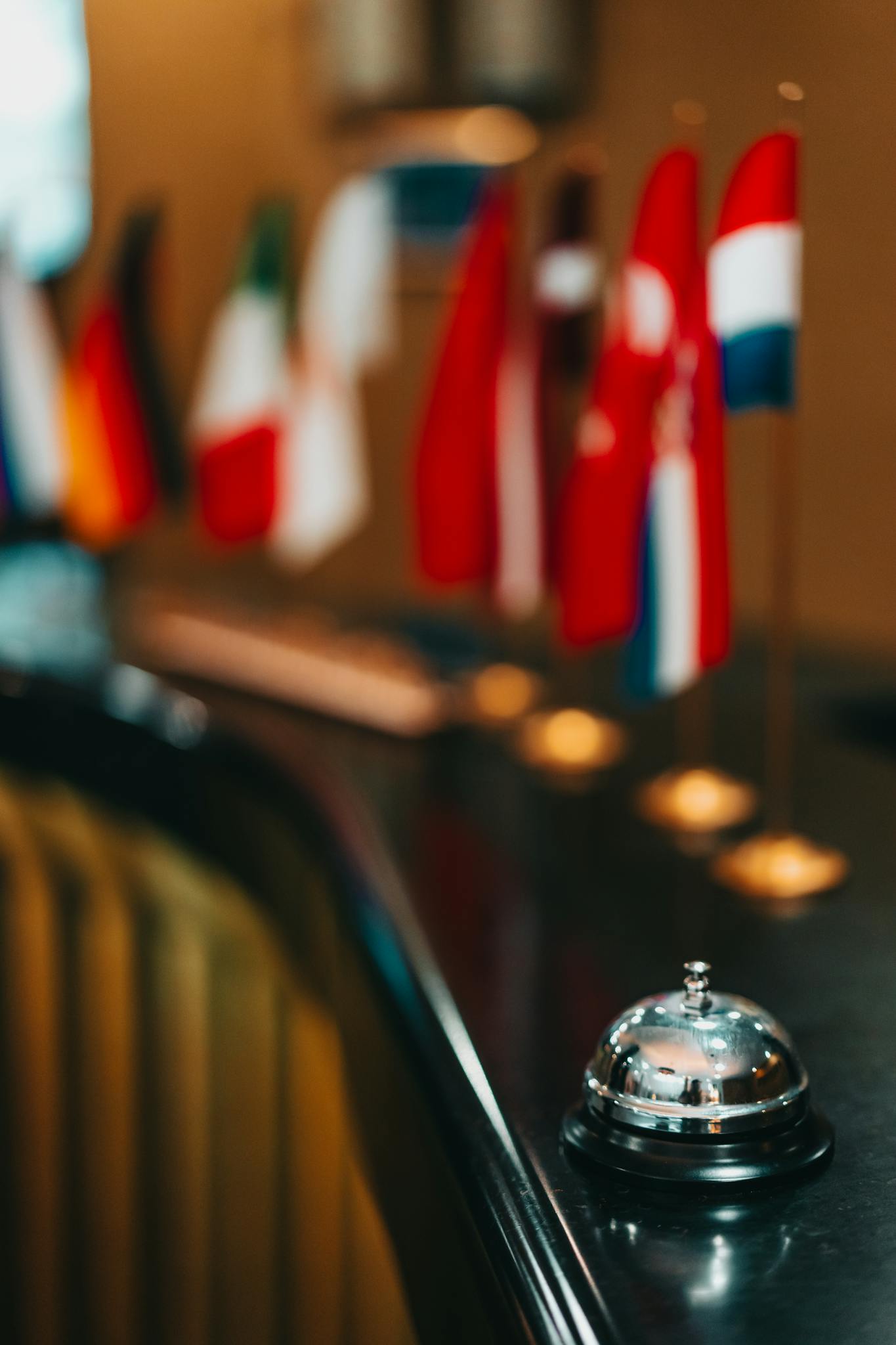Elegant hotel reception desk with a focus on a service bell and international flags in soft focus.